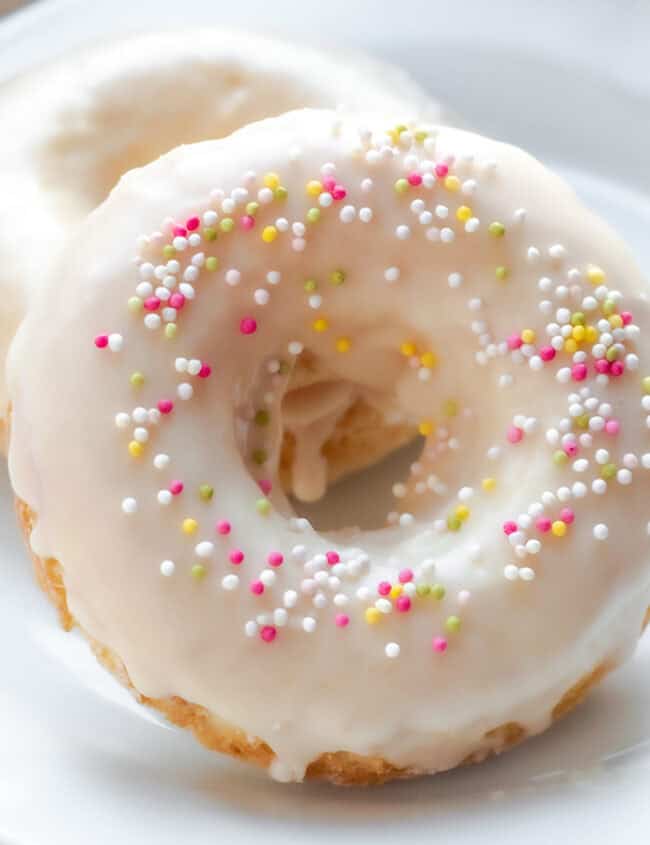 A close up image of Two Vanilla frosted donuts with colored sprinkles on a plate.