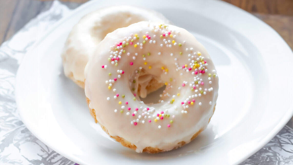 A close up image of Two Vanilla frosted donuts with colored sprinkles on a plate.