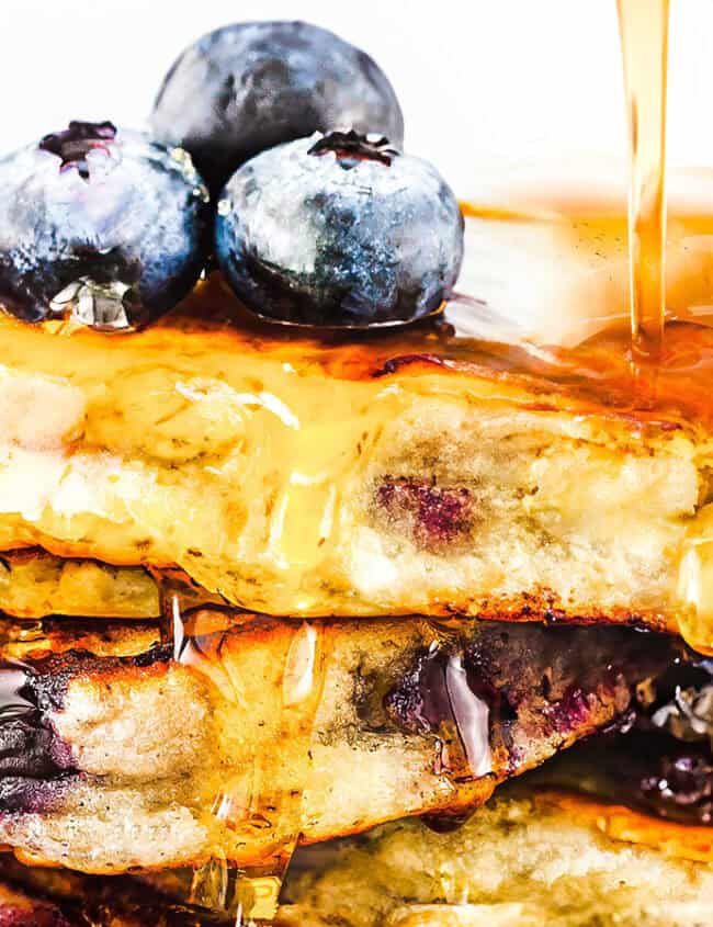 Blueberry pancakes dripping with syrup and topped with fresh blueberries.