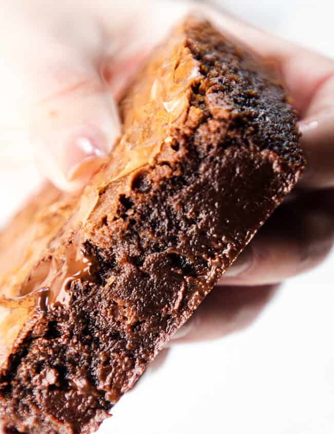 A close up image of a woman's hand holding a fudgy Chocolate Chip Chip Brownie.