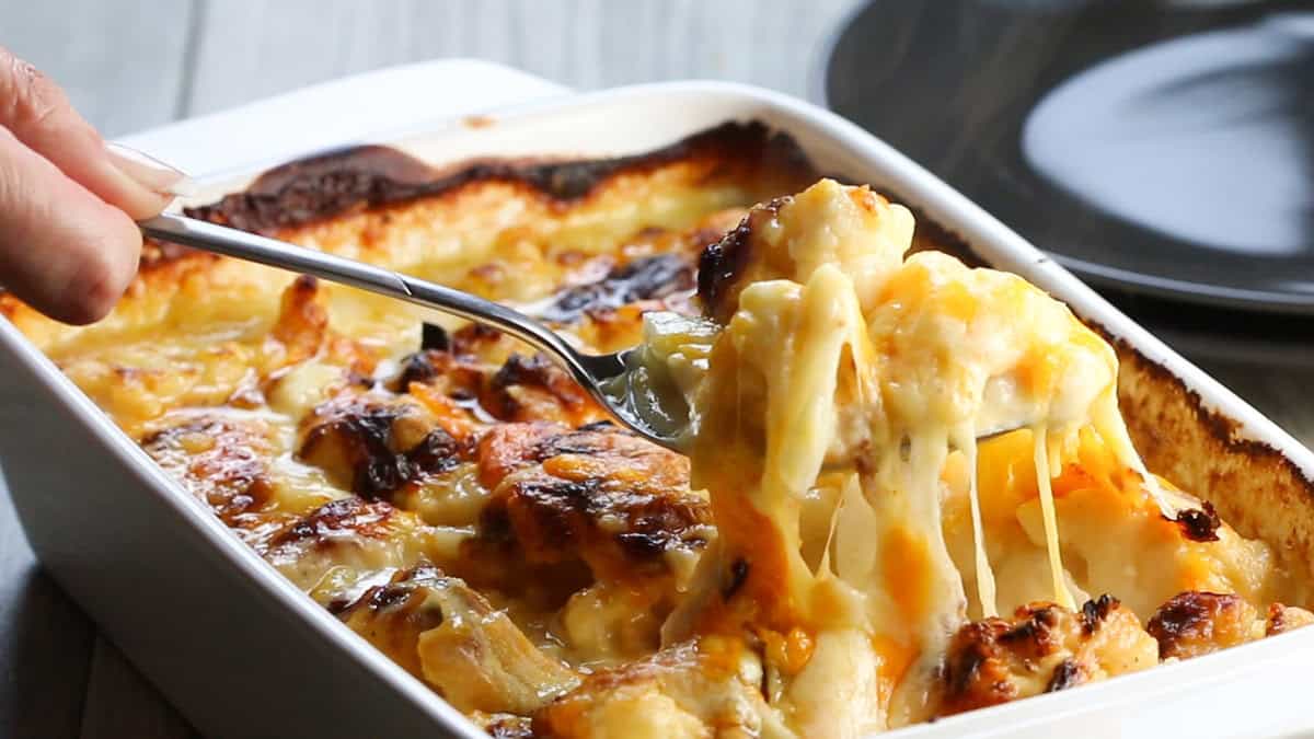 A spoon serving Cheesy Cauliflower from a pan.