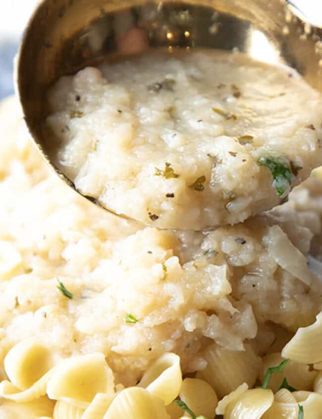 a spoonful of cauliflower sauce being added to a dish of pasta.