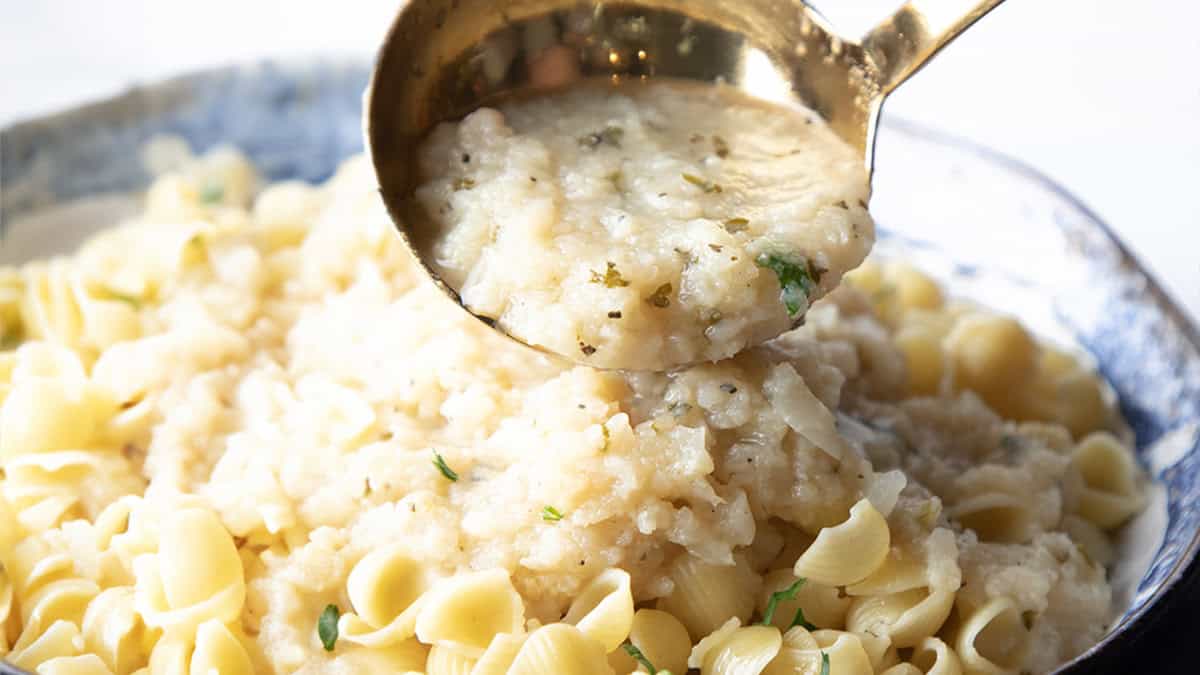 a spoonful of cauliflower sauce being added to a dish of pasta.