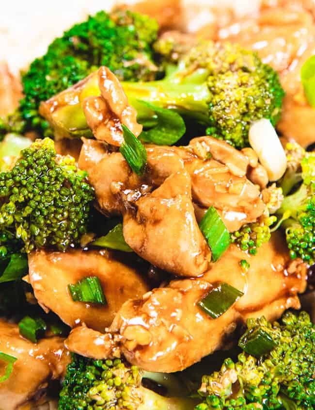 A chicken and Broccoli stir fry piled high on a white plate with chop sticks