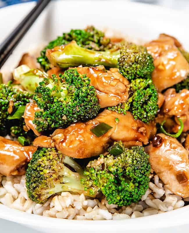 A chicken and Broccoli stir fry piled high on a white plate with chop sticks