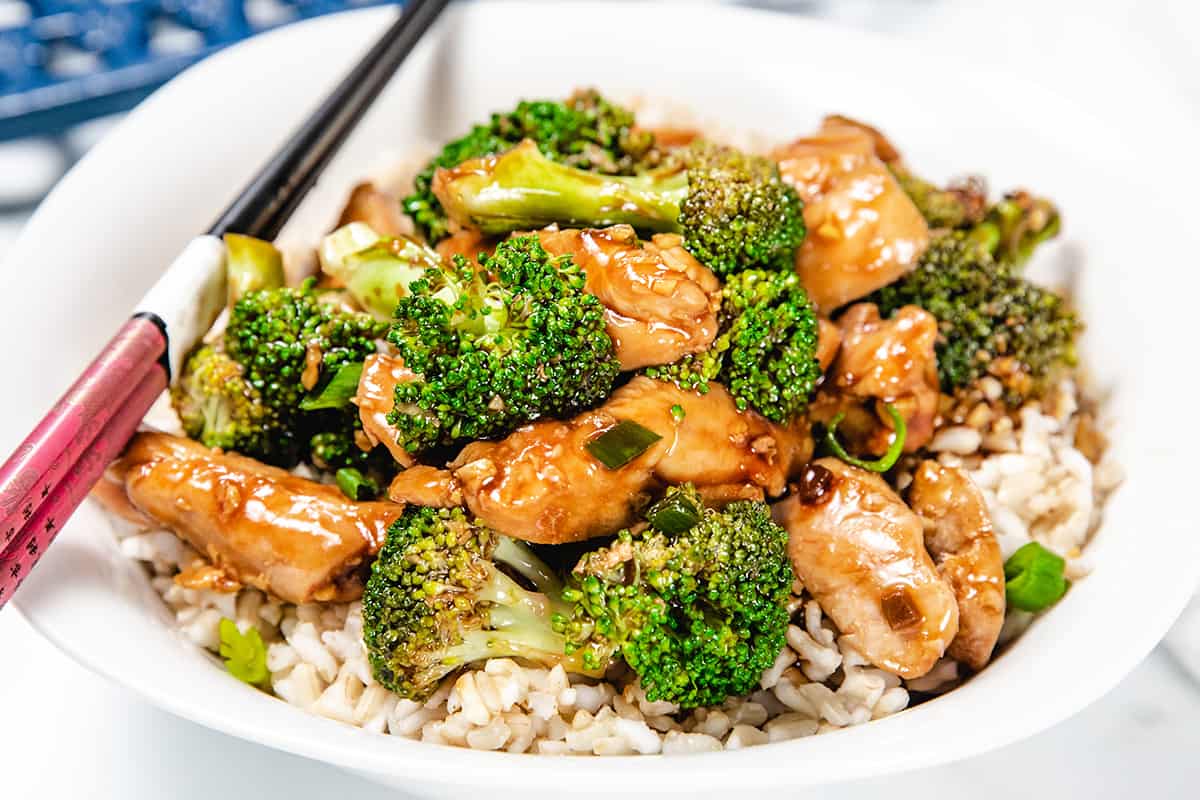 A chicken and Broccoli stir fry piled high on a white plate with chop sticks