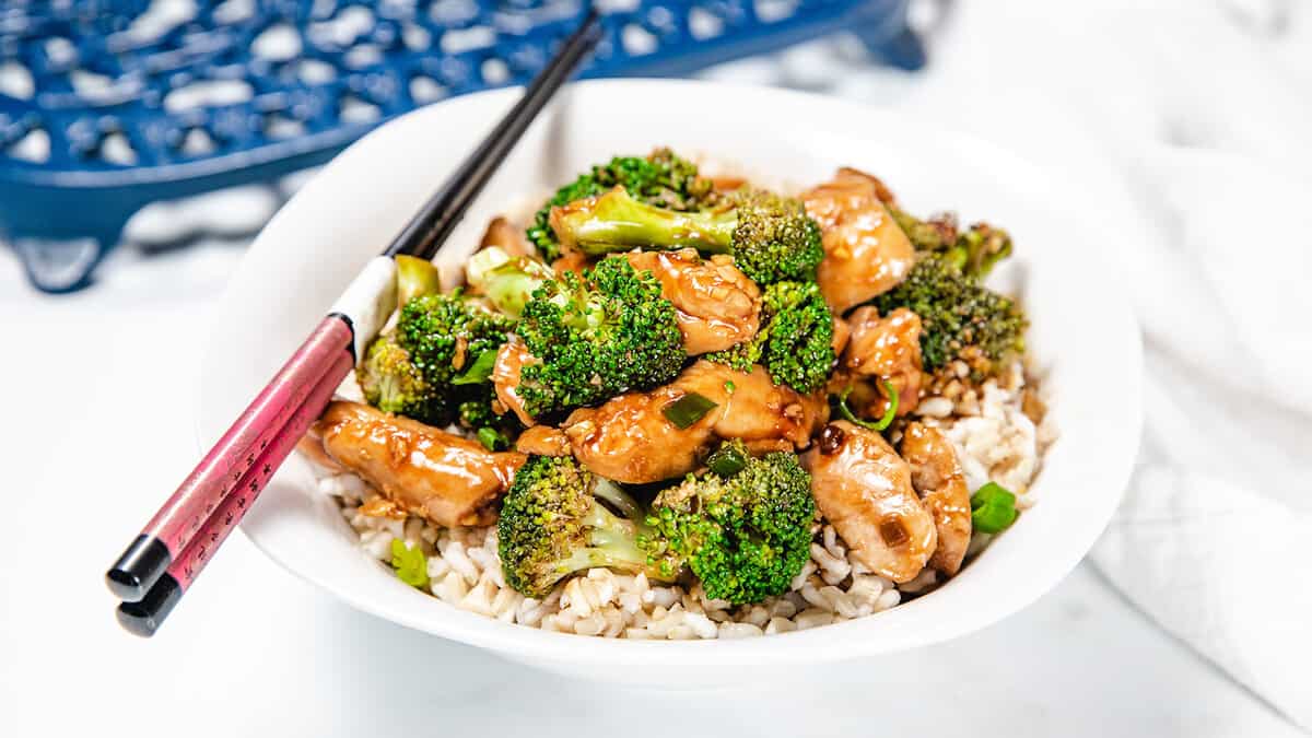 A chicken and Broccoli stir fry piled high on a white plate with chop sticks