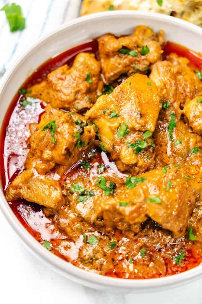 A close-up of Chicken Korma garnished with fresh cilantro in a white bowl.