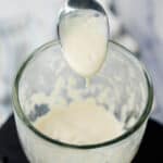 A spoon lifting a thick, creamy cashew paste from a blender jar.