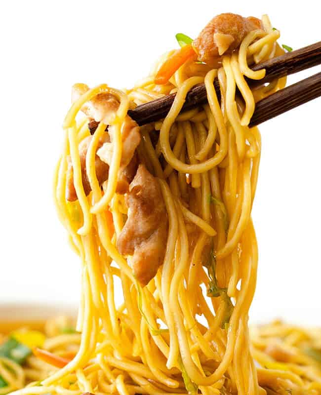 Chopsticks holding a chicken lo mein with noodles, vegetables, and chicken, set against a white background.