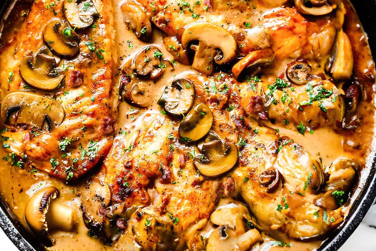 A close up image of A cast iron pan filled with chicken marsala and mushrooms.