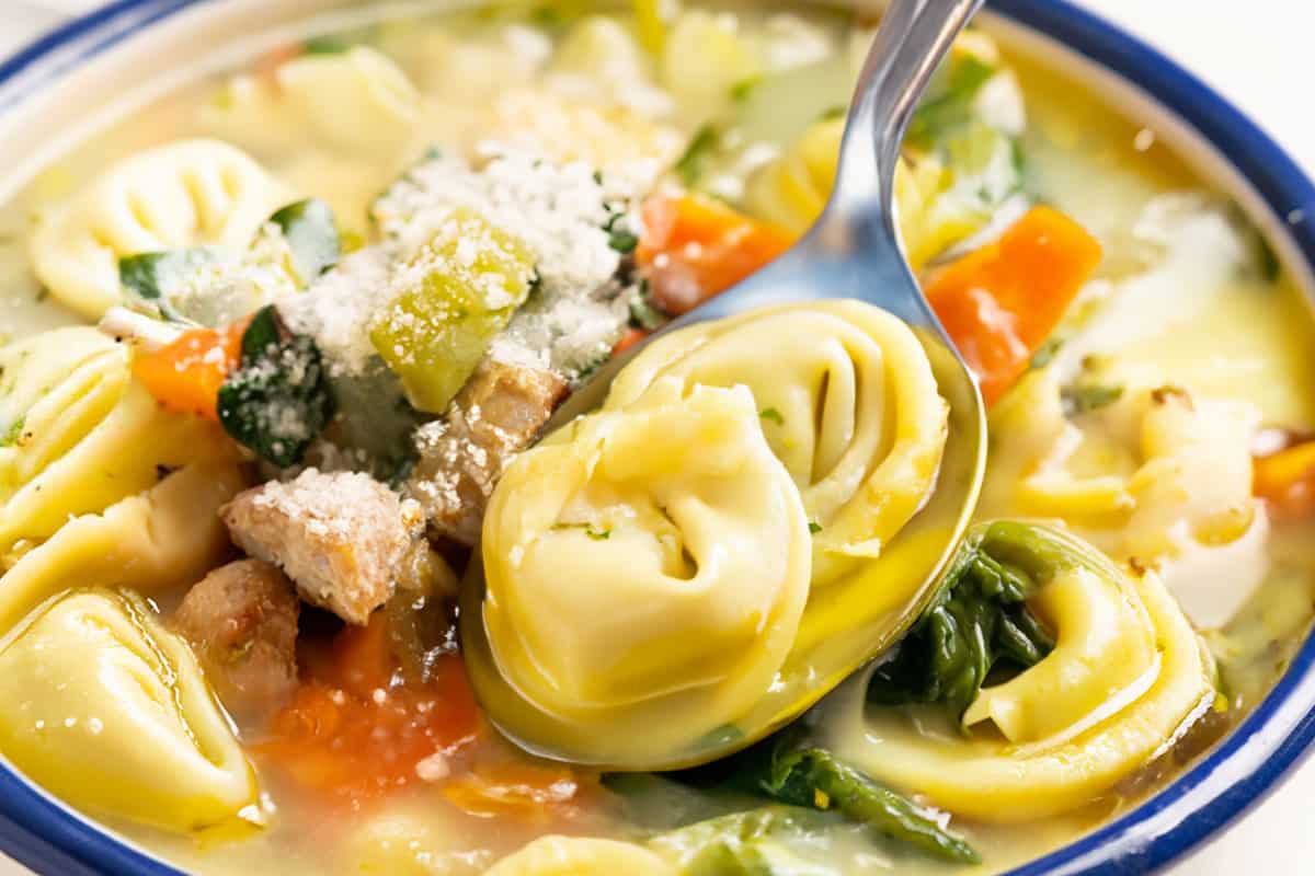 A bowl of comforting Chicken Tortellini Soup, with a spoon.
