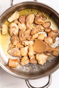 Sautéing bite-sized chicken pieces in a pot with a wooden spoon, showing golden-brown searing.