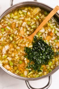 A pot of soup with diced vegetables and chopped parsley, wooden spoon included, indicating a meal in progress.