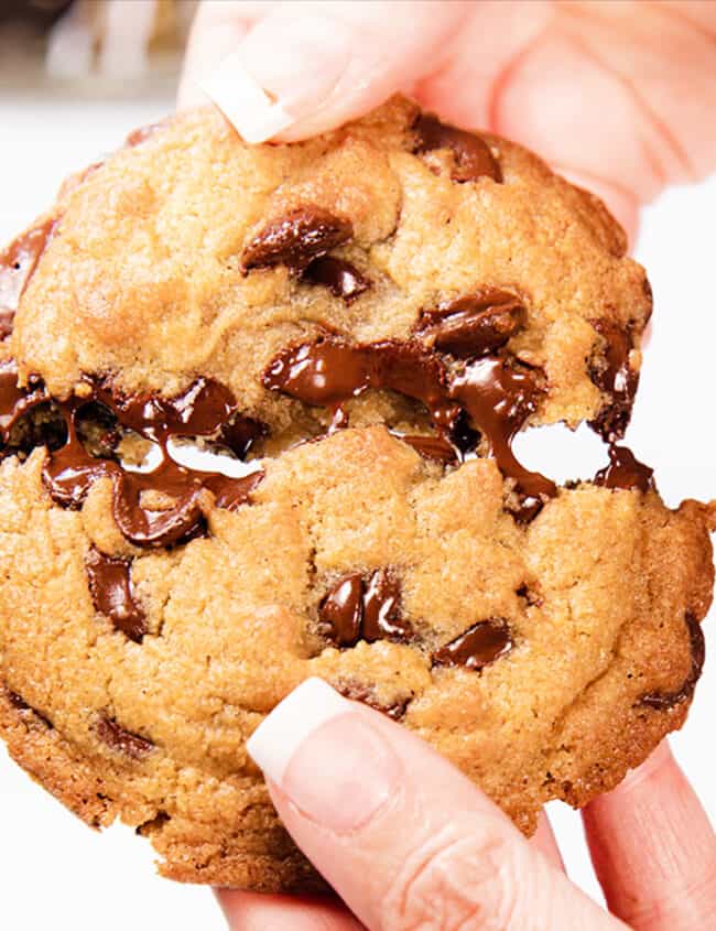 A chocolate chip cookie being broken in half.