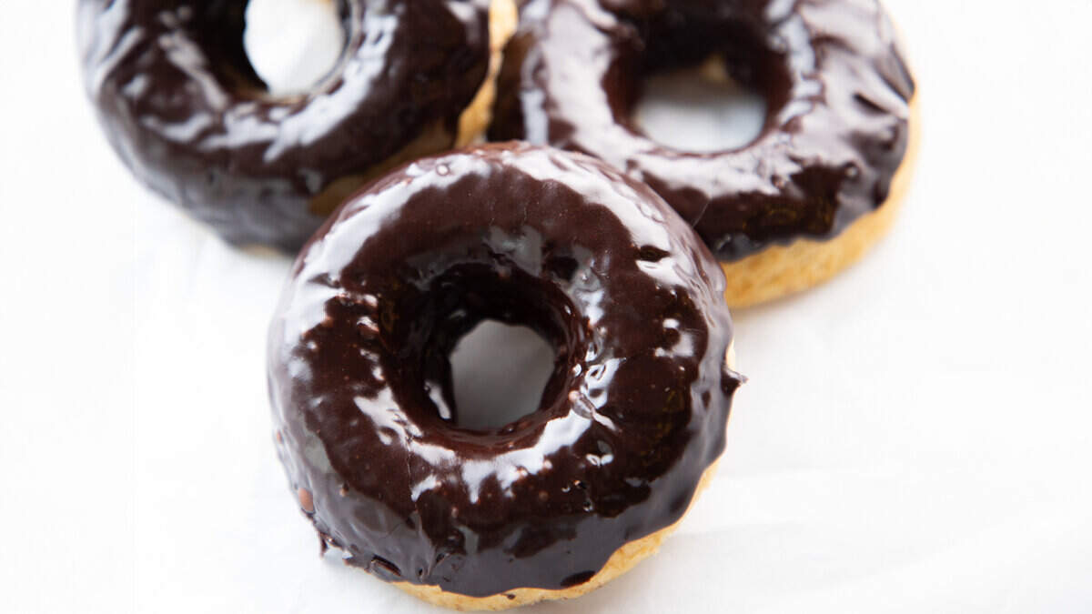 Three Chocolate frosted donuts with a white background.