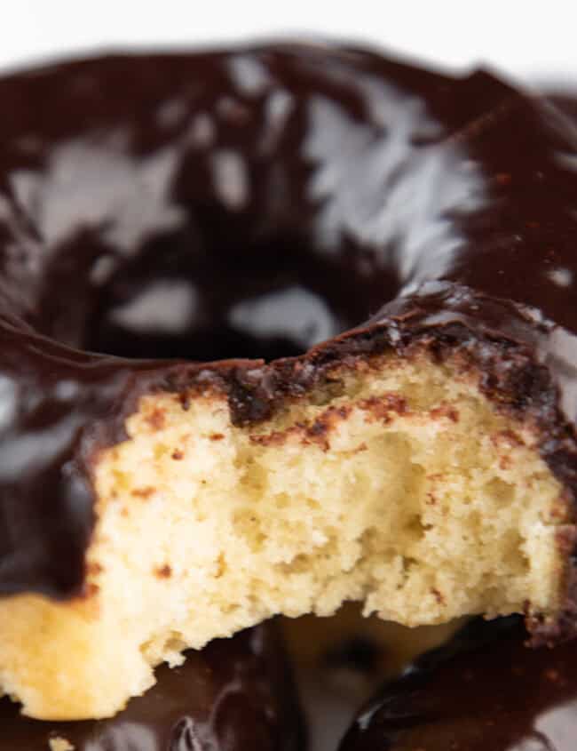 A pile of Chocolate frosted donuts with the top one missing a bite.