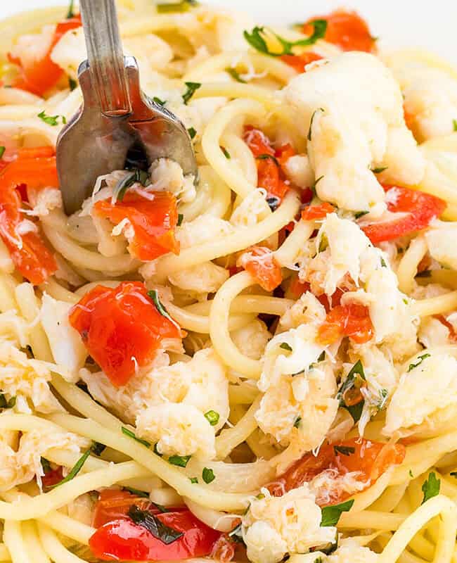 A close up image of a plate of spaghetti with crab, chopped parsley and red peppers.