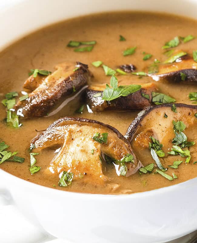 a close up image of golden mushroom soup in a bowl with slices of mushrooms on top.