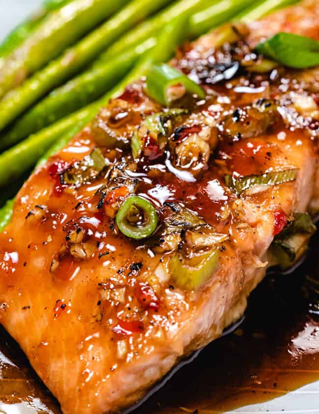 Glazed salmon on a plate with asparagus next to it.