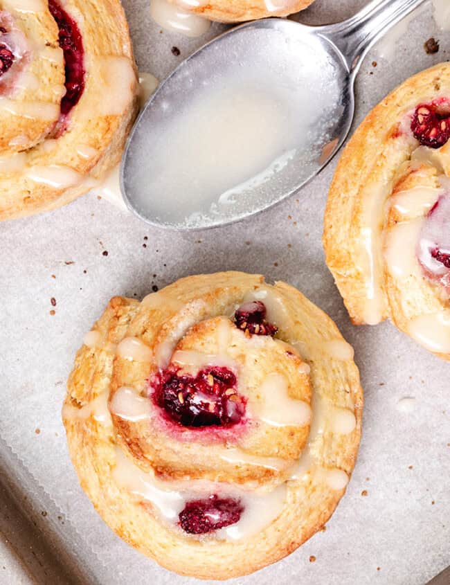 Close-up of raspberry swirled scones with icing on parchment paper, displaying the swirls of dough and berry filling.