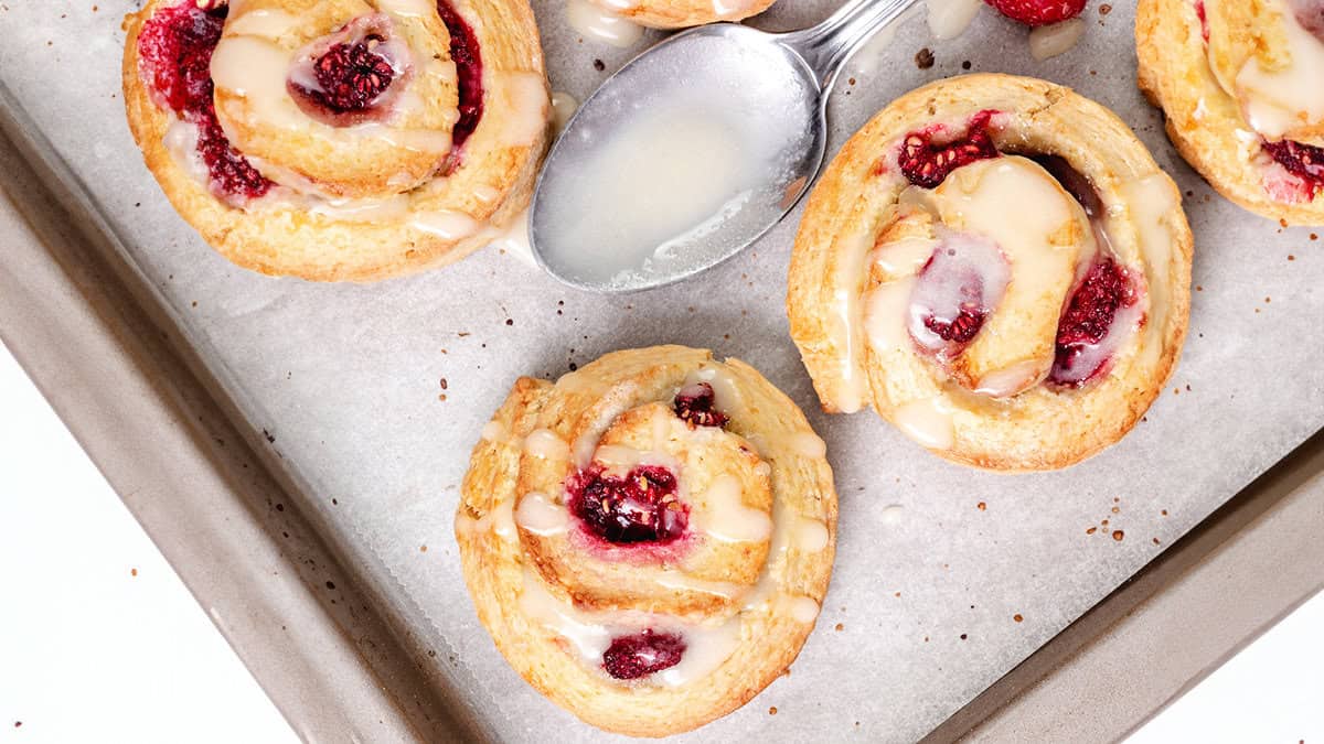 Close-up of raspberry swirled scones with icing on parchment paper, displaying the swirls of dough and berry filling.