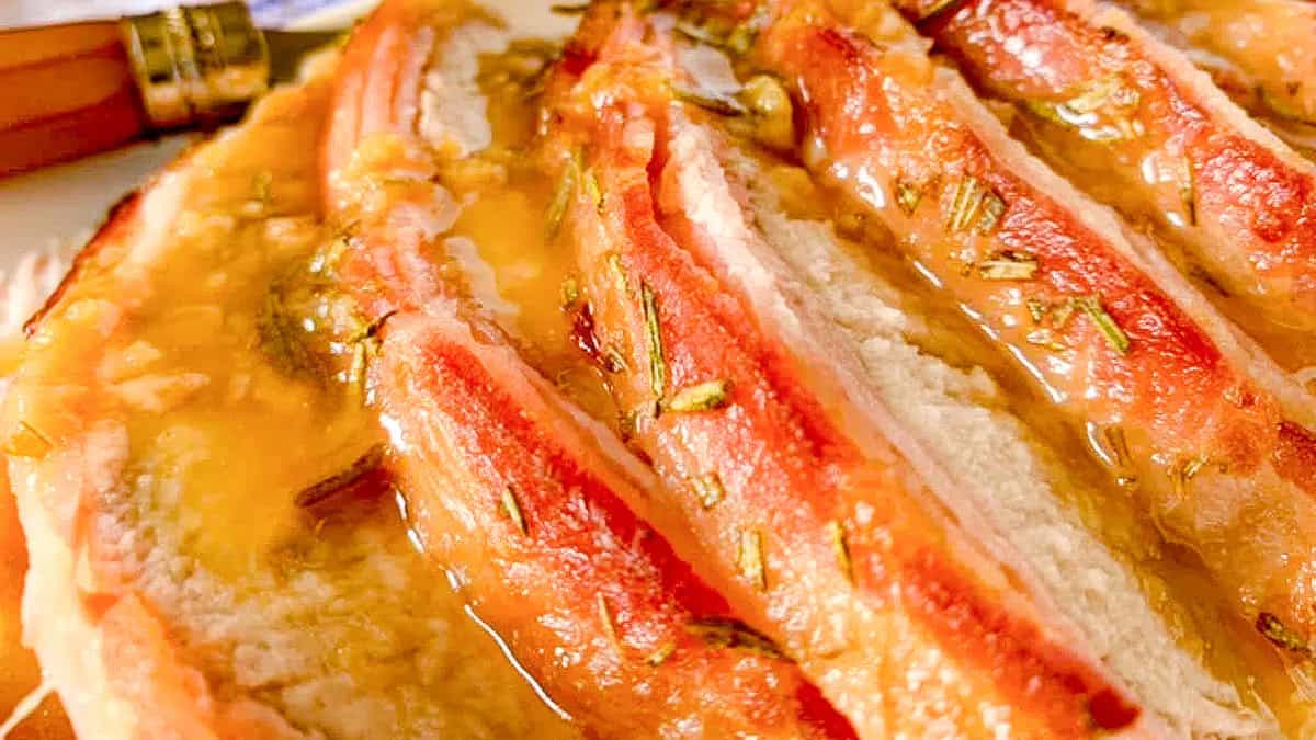 a close up image of Smoked Bacon Wrapped Pork Loin with a sauce going over it.