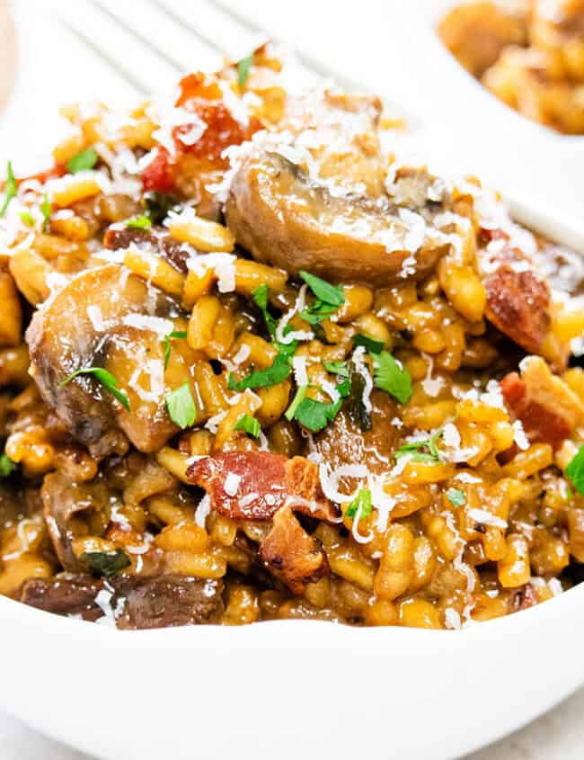 Mushroom and Bacon Risotto in a white bowl scattered with fresh herbs.