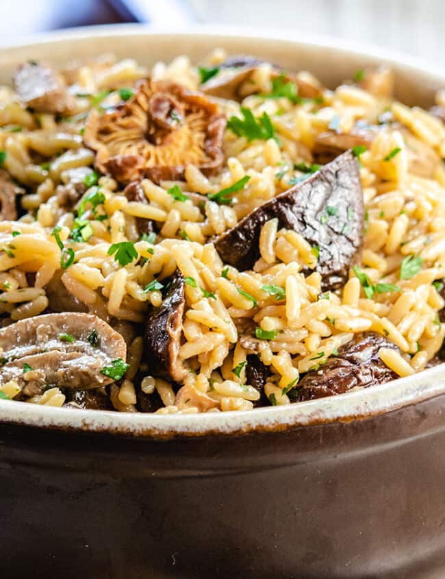 Mushroom rice pilaf in a serving dish with the lid behind it.