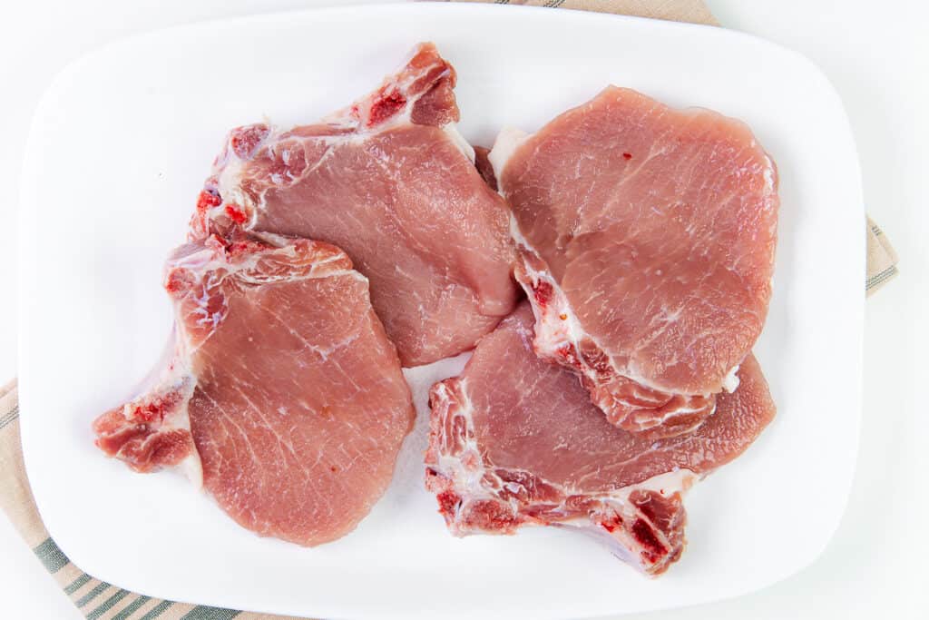 A platter of raw pork chops on a white plate.