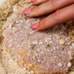 A pork chop being pressed into seasoned breadcrumbs preparing for frying.