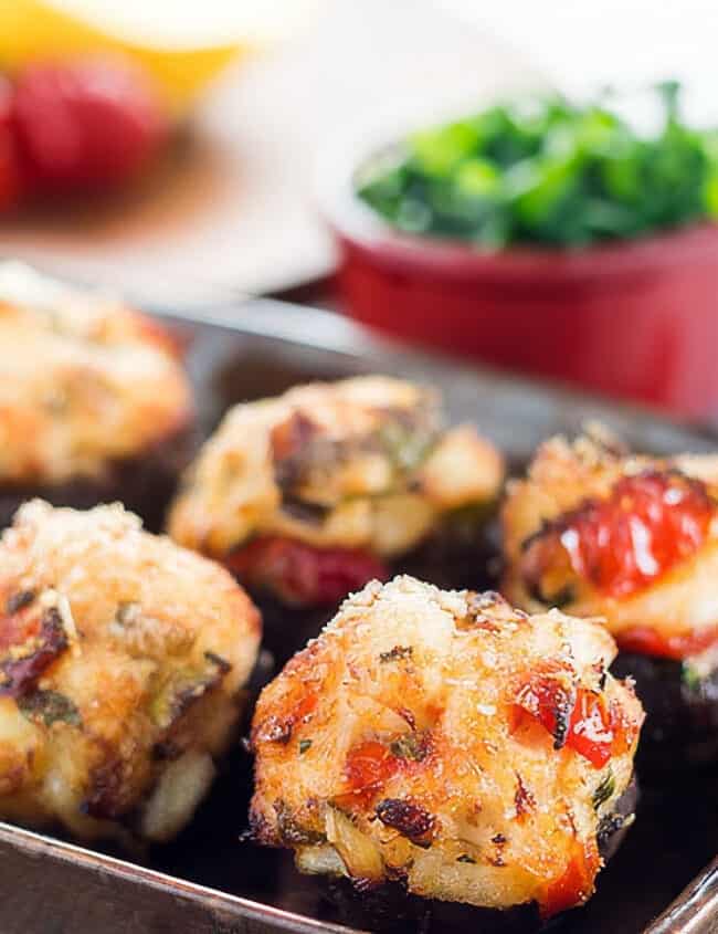 a close up image of Crab Stuffed Mushrooms on a plate with herbs in the background