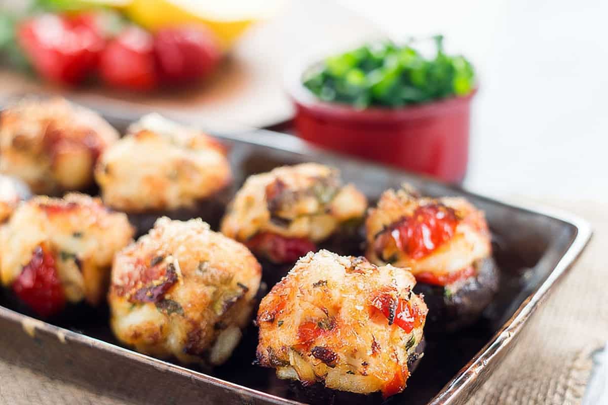 a close up image of Crab Stuffed Mushrooms on a plate with herbs in the background
