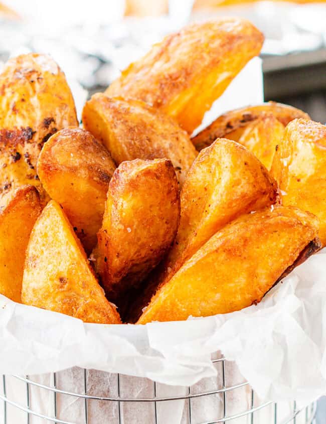 Seasoned Baked Potato Wedges in a metal serving basket sprinkled with salt.