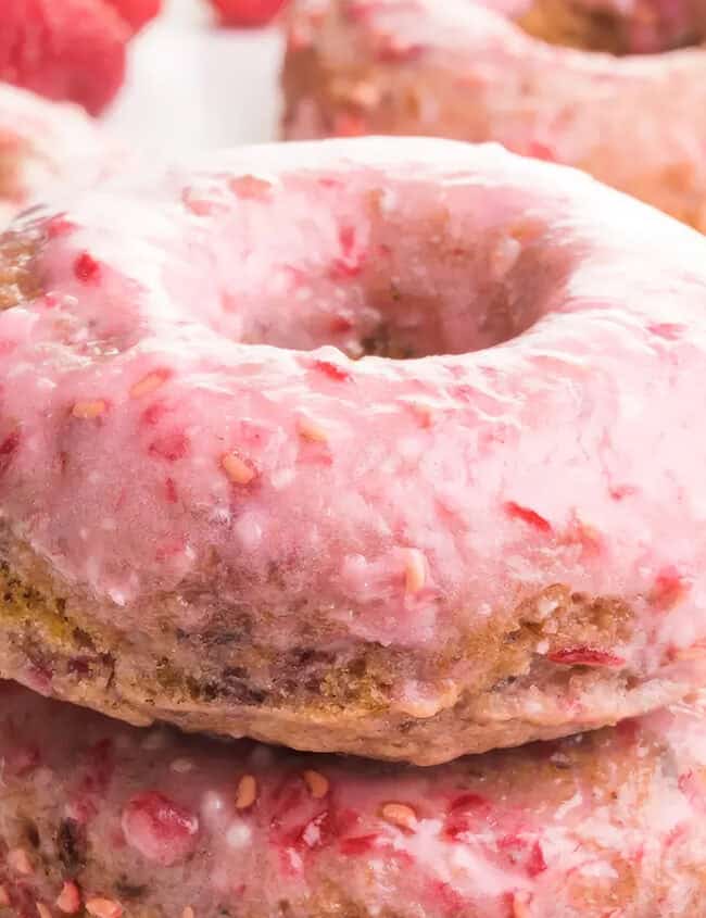 A close-up photo of a stack of glazed donuts with pink frosting on a white background.