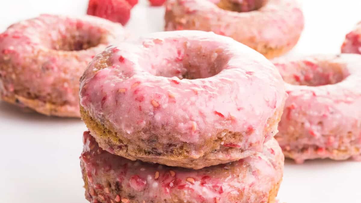 A close-up photo of a stack of glazed donuts with pink frosting on a white background.