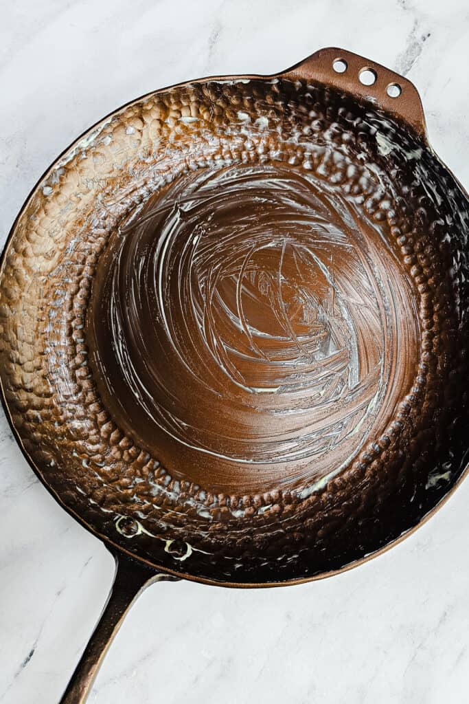 An overhead shot of a cast-iron skillet on a marble surface, coated with a glossy layer of melted butter.