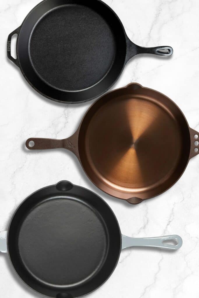 Three cast iron skillets on a marble surface.