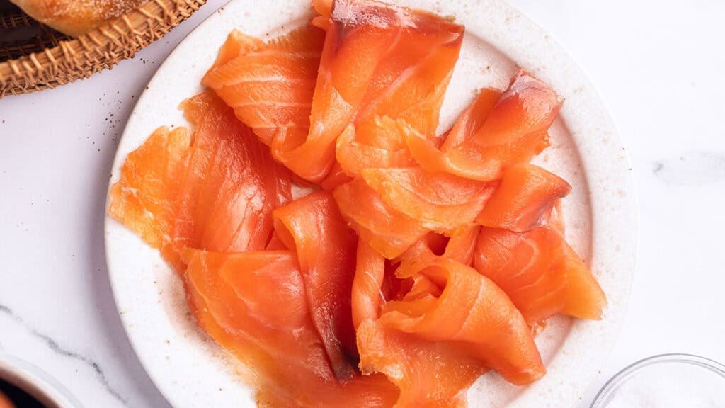 A white plate of sliced smoke salmon.