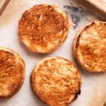 Two halved and toasted English muffins on a baking sheet.