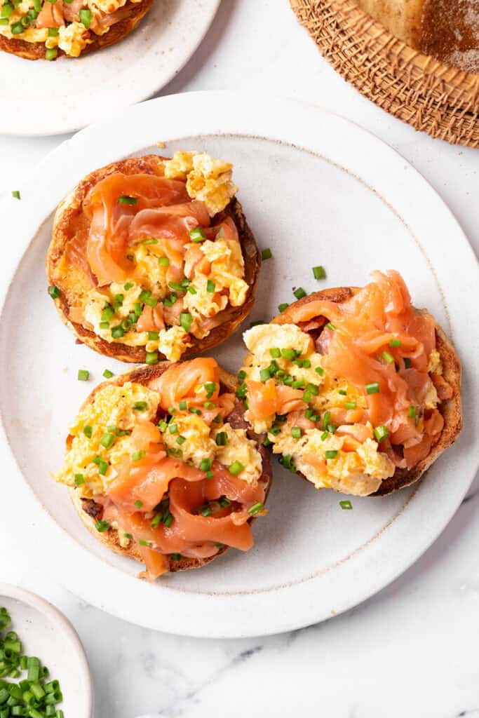 A breakfast plate with three halved English muffins topped with scrambled eggs and smoked salmon.