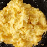 A close-up of a black pan filled with lightly scrambled eggs.