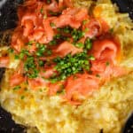 A skillet containing scrambled eggs with chopped smoked salmon and chives mixed in.