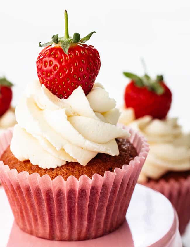 Three fresh strawberry cupcakes all topped with a swirl of whipped cream and a fresh strawberry.