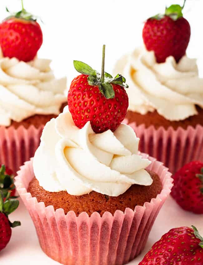 Three fresh strawberry cupcakes all topped with a swirl of whipped cream and a fresh strawberry.