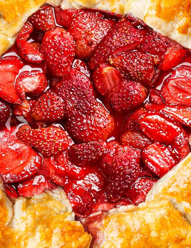 A strawberry pie sitting on a wire rack. While the image contains a pie crust design, it is more consistent with a galette or tart crust which typically has a more rustic, free-form edge than a pie crust.