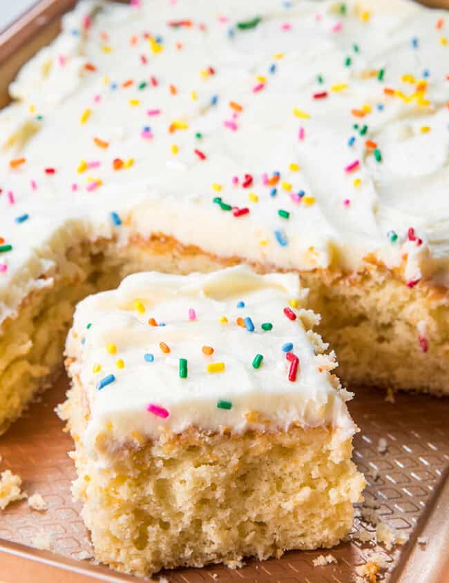 A sheet pan of vanilla cake with a slice cut out of it.