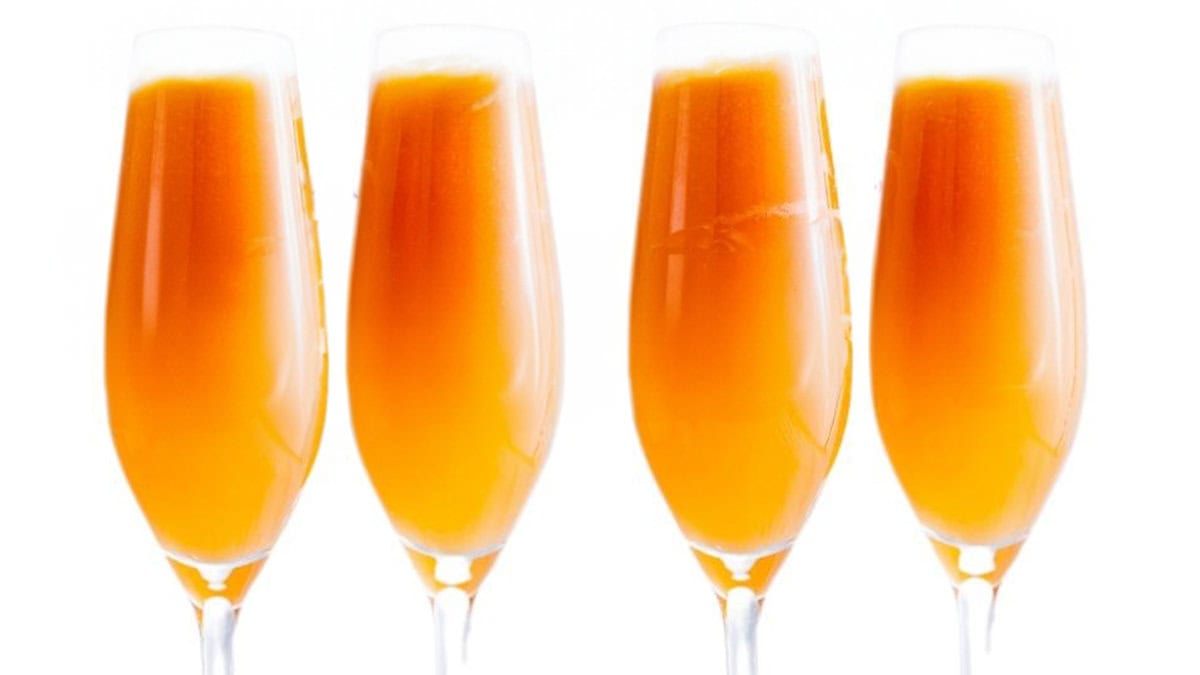 Four mimosas in long stem glasses with a white background.