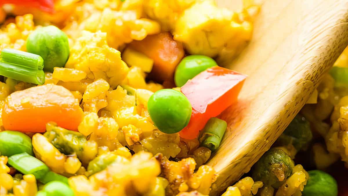A close up image of Vegan Fried Rice being served with a wooden spoon.