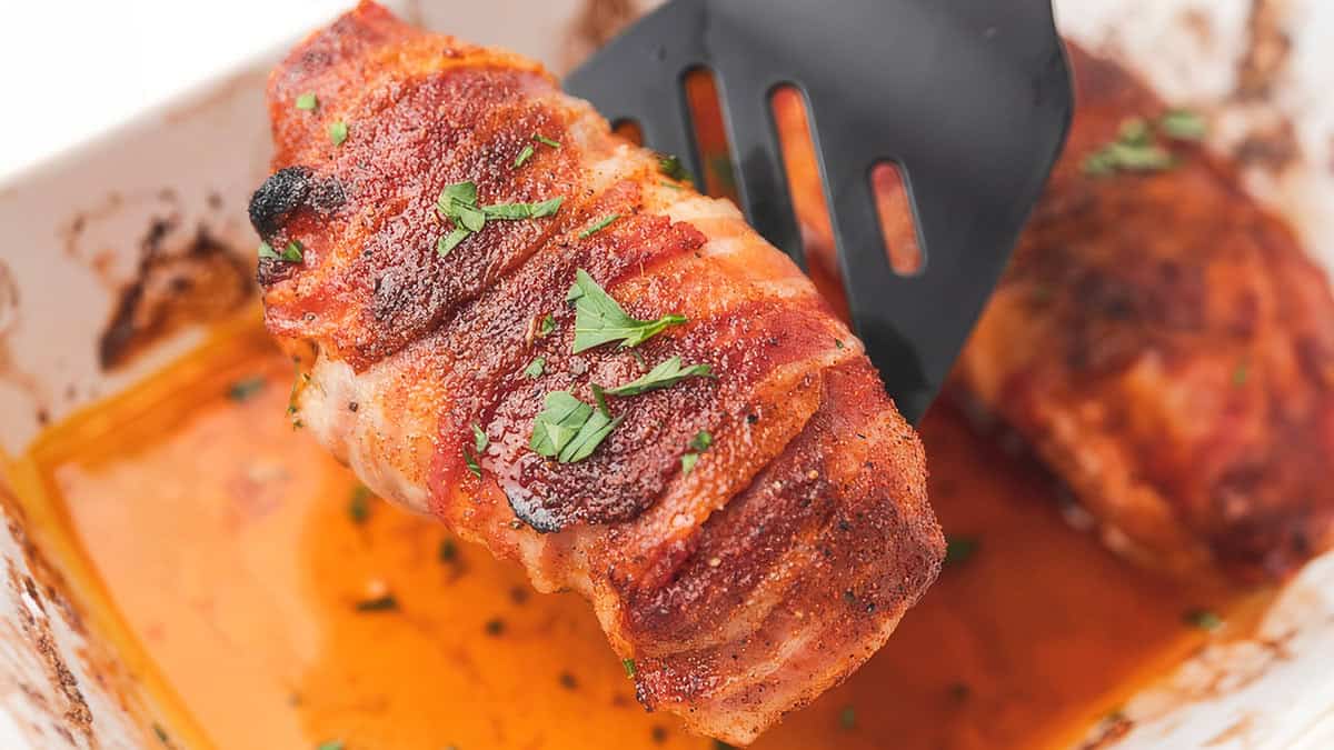 a close up image of a Bacon Wrapped Chicken Breast being served with a spatula.